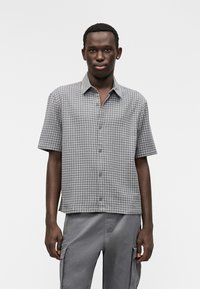 Πουκάμισο με κοντά μανίκια και κουμπιά, σε γκρι και μαύρο καρό μοτίβο, κατασκευασμένο από ελαφρύ ύφασμα. Ίσια ποδόγυρος και άνετη εφαρμογή.