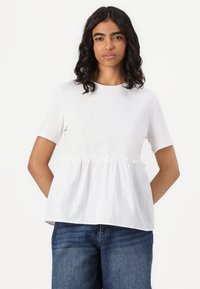 Hvit kortermet T-skjorte med samlet midje, laget av myk bomullsblanding, sammen med mørkeblå jeans.
