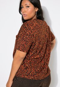 Top de manga corta con estampado de leopardo marrón y un corte relajado, que presenta acentos en negro y dorado en el patrón, hecho de una tela suave y texturizada.