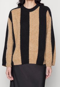 Beige und schwarz gestreifter Pullover aus weichem, strukturiertem Stoff. Hat einen runden Ausschnitt und weite Ärmel, mit einer lockeren Passform.