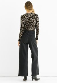 Top a maniche lunghe con una stampa leopardata in tonalità di marrone e nero abbinato a jeans neri a vita alta e gamba larga, con tacchi neri.