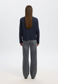 Narančasta majica dugih rukava s okruglim izrezom u mornarsko plavoj boji uparena s visokim strukom i širokim krojem sivih traperica. Glatka tekstura i minimalni dizajnerski detalji.