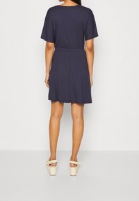 Granatowa sukienka z krótkim rękawem, z elastyczną talią i długością sięgającą do połowy uda, zestawiona z jasnymi platformami.