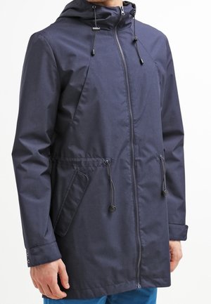 Granatowa kurtka z kapturem, zamkiem z przodu, regulowanymi sznurkami w talii, bocznymi kieszeniami oraz mankietami na guziki noszona przez osobę.