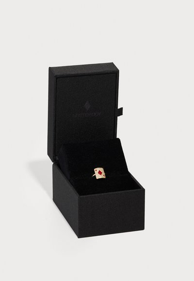 Gold ring in a black jewelry box; features a diamond-shaped red accent and textured surface. Compact and box-shaped design.