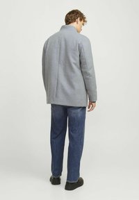 Abrigo gris de mezcla de lana con cuello alzado, corte recto y mangas largas, combinado con jeans azules y zapatos negros, visto desde atrás.