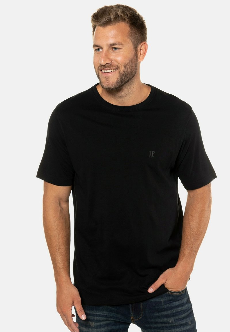 Zwart T-shirt met korte mouwen van zacht materiaal, met een ronde halslijn en een subtiele logo op de borst. Gestyled met een blauwe spijkerbroek.