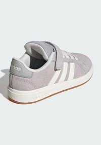 Sneaker en nubuck gris avec une semelle en caoutchouc blanc, dotée d'une sangle Velcro, de rayures blanches sur le côté et d'une languette en tissu texturé.