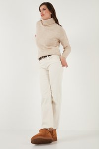 Pulover bej cu guler înalt, pantaloni crem cu croi drept și botine maro din suede cu tălpi texturate, purtând un curea simplă.