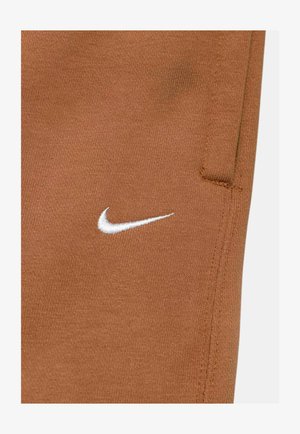 Braune Nike Jogginghose aus einem glatten Material. Mit einem weißen Logo und Taschen, sowie sauberen Nähten an den Seiten.