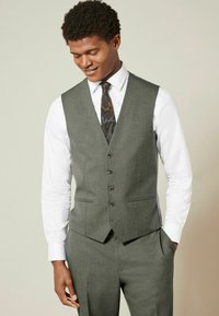 Chaleco de tela gris con cinco botones, llevado sobre una camisa blanca y una corbata con estampado. El chaleco tiene un corte ajustado y bolsillos laterales.