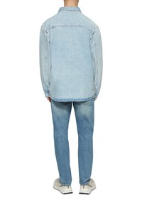 Jasnoniebieska kurtka dżinsowa z długimi rękawami, kołnierzem i detalem na plecach, w połączeniu z pasującymi jasnoniebieskimi dżinsami i kremowymi sneakersami.