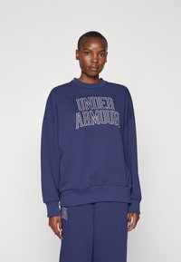 Mørkeblå sweatshirt lavet af bomuldsblanding med ribbet krave og manchetter. Har "Under Armour" logo i fed hvid skrift.