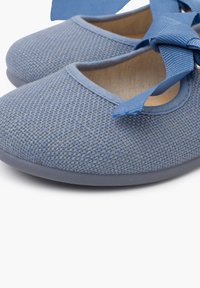 Zapatos de tela azul claro con superficie texturizada, punta redonda y una cinta a juego atada en la parte superior. Suela blanda para mayor comodidad.