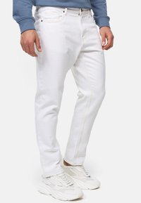 Jeans de denim blanco con corte recto, que presentan costuras en contraste y detalles en las costuras laterales, combinados con zapatillas de color claro.