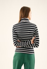Black and white striped long-sleeve top with a mock neck, ribbed texture, fitted design, worn with green pants.