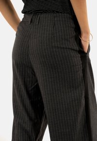 Pantalons à rayures charbon gris avec une coupe décontractée. Dotés d'une taille avec plis et de poches latérales. Fabriqués à partir d'un tissu doux.