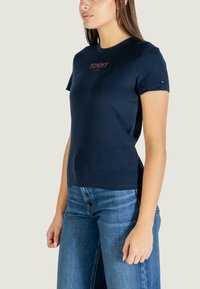 Tmavě modré bavlněné tričko s krátkými rukávy, zdobené červeným logem "TOMMY" a malým praporkovým detailem na rukávu. Přiléhavý střih.