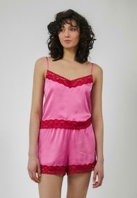 Conjunto de top de satén rosa y pantalones cortos, que presenta un borde de encaje rojo a lo largo del escote y el dobladillo, exhibiendo una textura suave y un diseño delicado.