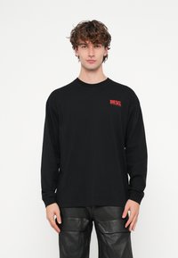 Melna garām piedurknēm kokvilnas T-krekls ar nelielu sarkanu "DIESEL" logotipu uz krūtīm. Vienkāršs dizains ar brīvu piegriezumu.