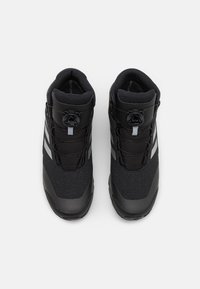 Svart högskurna skor med textilmaterial, en slät gummisula och BOA-snörningssystem. Har två grå ränder på sidan.