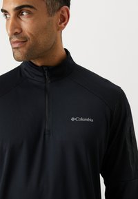 Schwarzer Reißverschluss-Pullover von Columbia, mit einem Reißverschluss in Viertellänge, glatter Textur und einem dezenten Logo auf der linken Brust.