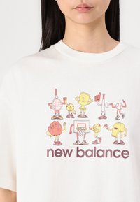 Balta grafikos marškinėliai su žaismingais sporto tematikos personažų piešiniais, apačioje bold purple spalvos tekstas "new balance".