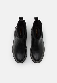 Czarne skórzane botki za kostkę z teksturowanym materiałem wokół otworu, kontrastującymi białymi szwami oraz pętelkami ułatwiającymi zakładanie.