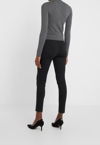 Grå kroppsnära långärmad topp i kombination med svarta slim-fit byxor och svarta högklackade skor. Enkelt design; inga synliga mönster eller logotyper.