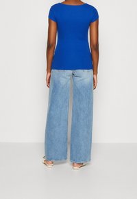 Royal blue ribbed top with short sleeves paired with wide-leg light blue denim jeans. Visible seams and relaxed fit. White footwear.