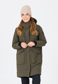 Olivgrön, lång parka med dragkedja och knappstängning, som har två stora framfickor och huva. Mjuk beige stickad mössa på modellen.