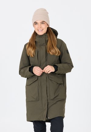 Oliven grøn, lang parka med frontlynlås og knaplukning, der har to store forlommer og en hætte. Blød beige strikket hat på modellen.