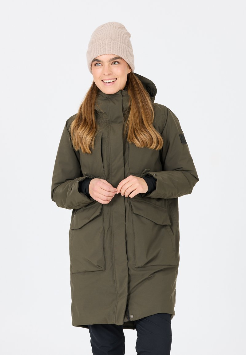 Olivgrön, lång parka med dragkedja och knappstängning, som har två stora framfickor och huva. Mjuk beige stickad mössa på modellen.