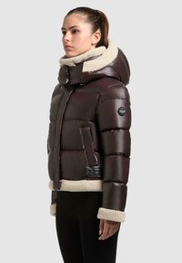 Braune Pufferjacke mit Kapuze, ausgestattet mit einem cremefarbenen Kunstfellkragen, horizontaler Steppung und einerseitentasche mit schwarzem Akzentpaneel.