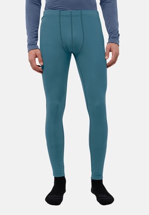 Man draagt teal aansluitende legging, zwarte sokken en een blauw shirt met lange mouwen, staand tegen een witte achtergrond.