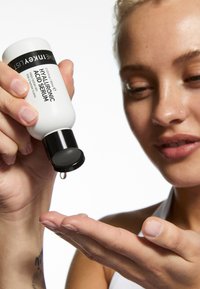 Hyaluronsyreserum i en hvid flaske med et sort låg. En dråbe serum ses på en hånd, der viser en klar, let konsistens.
