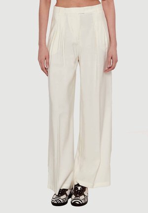 Pantaloni palazzo plissettati realizzati in morbido tessuto crema con vita alta. Indossati con scarpe a fantasia in bianco e nero.