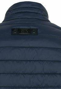 navyblaues Steppjacke mit hohem Kragen, horizontal gestepptem Design, gummiertem Logo-Patch und Druckknöpfen am Hals.