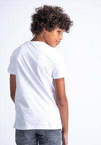 Weißes Baumwoll-T-Shirt mit kurzen Ärmeln, lockerer Passform und klassischem Rundhalsausschnitt, getragen mit grauen Jeans, von hinten betrachtet.