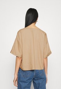 Top beige de manga corta con un corte holgado, tejido texturizado y escote redondo, combinado con jeans de mezclilla azules con detalles de costura.
