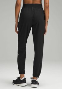 Black athletic pants with a tapered design, elastic waistband, and cuffs. Made of lightweight fabric. Worn with black and white sneakers.