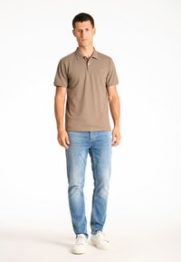 Herrpolo i taupe med krage och korta ärmar. Kombinerad med ljusblå jeans och vita sneakers. Enkel logotyp på bröstet.