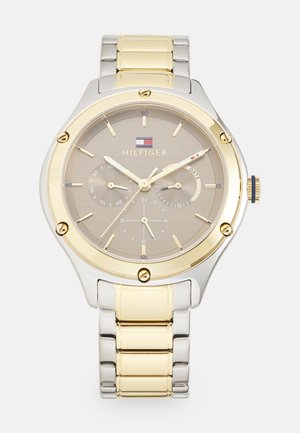 Montre en métal argenté et doré avec un cadran rond, un cadran gris clair, des accents dorés, trois sous-cadrans, et un bracelet texturé.