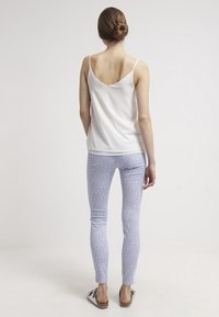 Top blanco sin mangas con un escote bajo, combinado con leggings de patrón azul claro. Los leggings tienen una textura suave y un diseño ajustado.