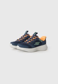 Baskets slip-on Skechers bleu marine avec lacets orange, semelles épaisses blanches et logo et accents vert fluo.