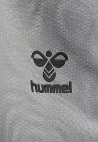 Il tessuto grigio presenta un motivo testurizzato con un logo nero di un'ape stilizzata sopra la parola "hummel" in lettere grasse.