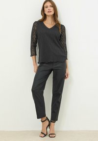 Sort top med spidse ærmer i trekvart længde, en V-udskæring, parret med sorte tætsiddende bukser og sorte strop sandaler. Glatte teksturer og elegant design.