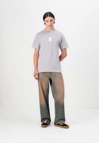 Lysegrå bomulds t-shirt med et hvidt grafisk design på brystet, kombineret med løstsiddende, lysnede denim jeans og sorte sneakers.