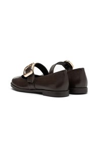 Zapatos Mary Jane de cuero marrón oscuro con hebillas doradas anchas y tacones bajos, mostrados sobre un fondo blanco, inclinados para mostrar la parte trasera y lateral.