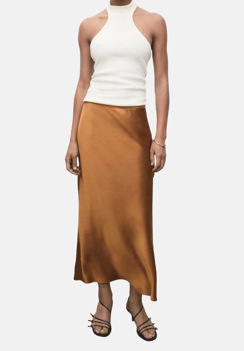 Top blanco de cuello halter combinado con una falda maxi marrón de satén fluido, que presenta una textura suave y un diseño hasta el tobillo. Sandalias negras con tiras.